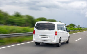 A white 7-seater MPV driving along a highway