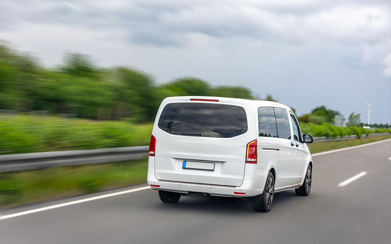 A white 7-seater MPV driving along a highway